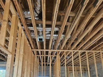 Framed interior of a house under construction, showing exposed wooden studs and ceiling joists.