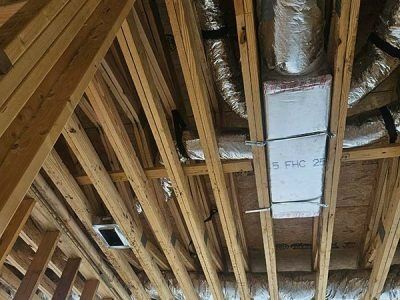 Exposed wooden roof framing with insulation and HVAC ductwork in an attic under construction