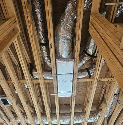 Exposed attic framing with silver HVAC ducting and a white air vent box between wooden rafters