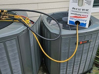 Two outdoor air conditioning units connected by yellow and black hoses, with a service test meter on one unit.