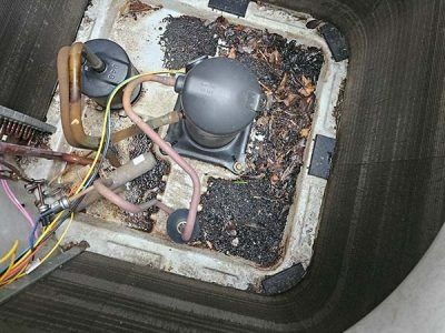 Damaged HVAC unit interior with corroded wiring, debris, and a gray compressor inside a metal cabinet