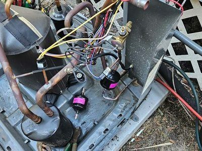 Close-up of tangled wires and copper pipes inside a mechanical unit with two magenta components.