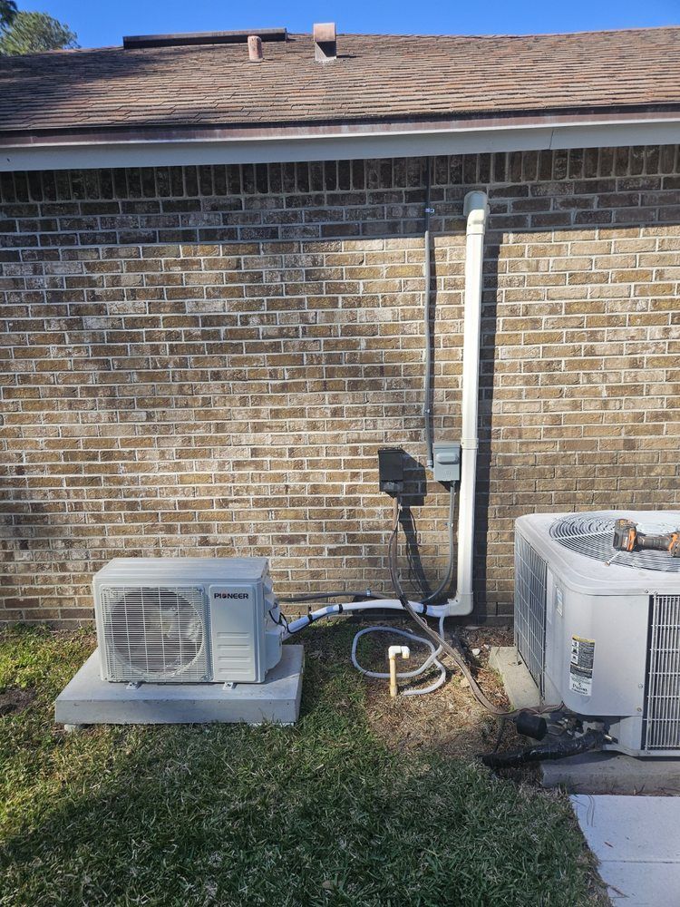 Outdoor HVAC units beside a brick house, with a white downspout and grassy yard.