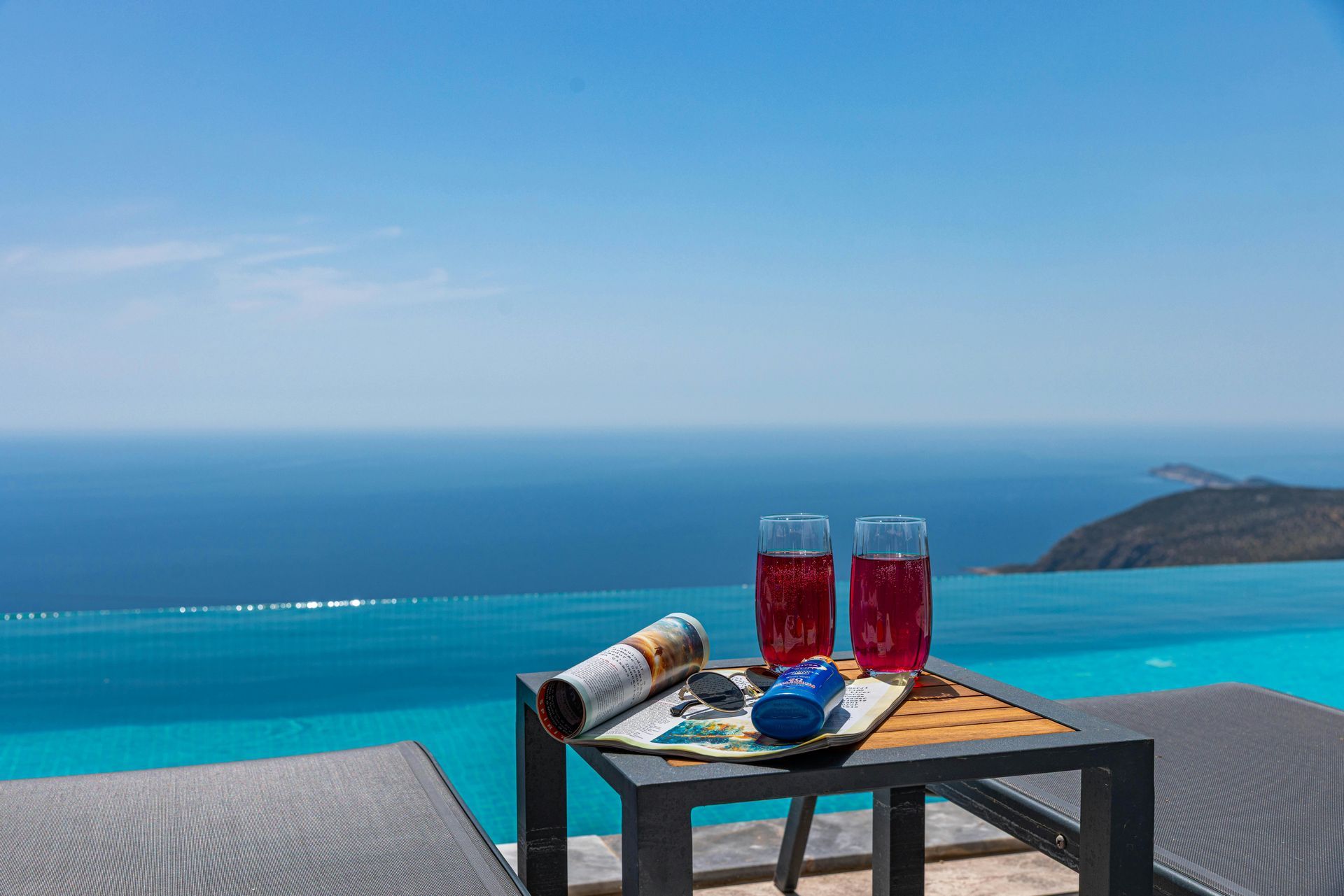 Two pink drinks on a table by a pool overlooking the ocean. Sunny day.