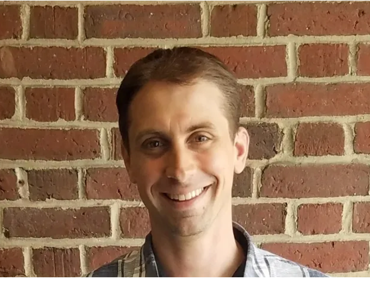 A man is smiling in front of a brick wall