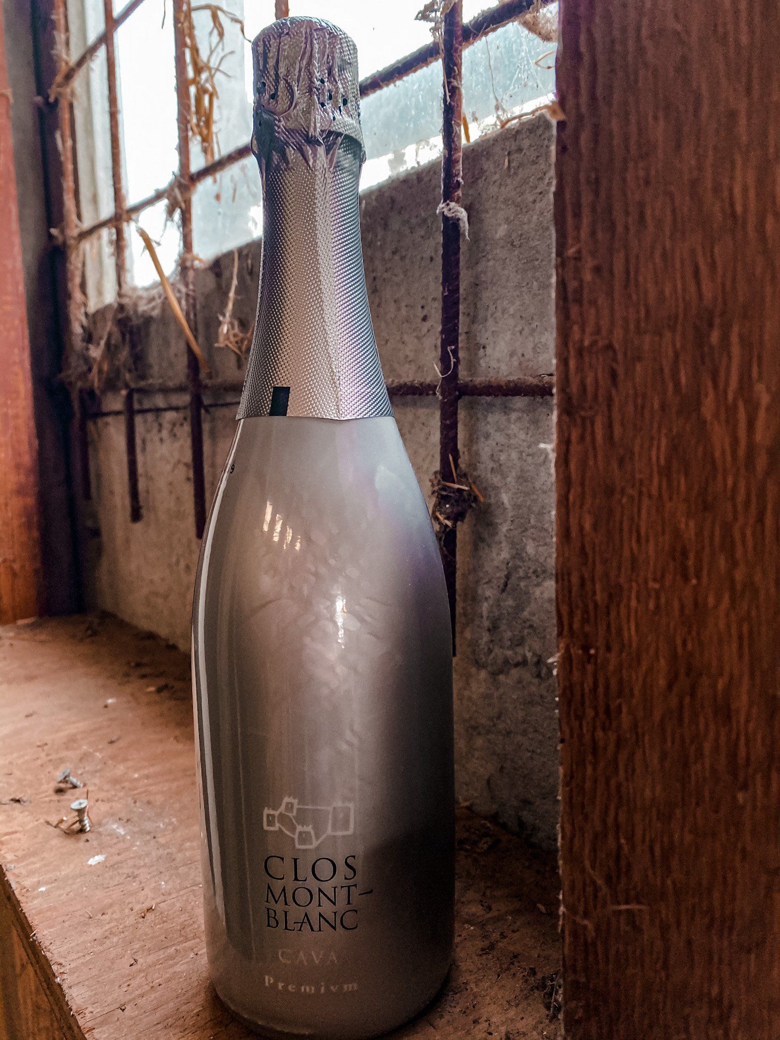 Een fles mousserende wijn Clos Son Blanc staat op de vensterbank naast een raam met tralies.