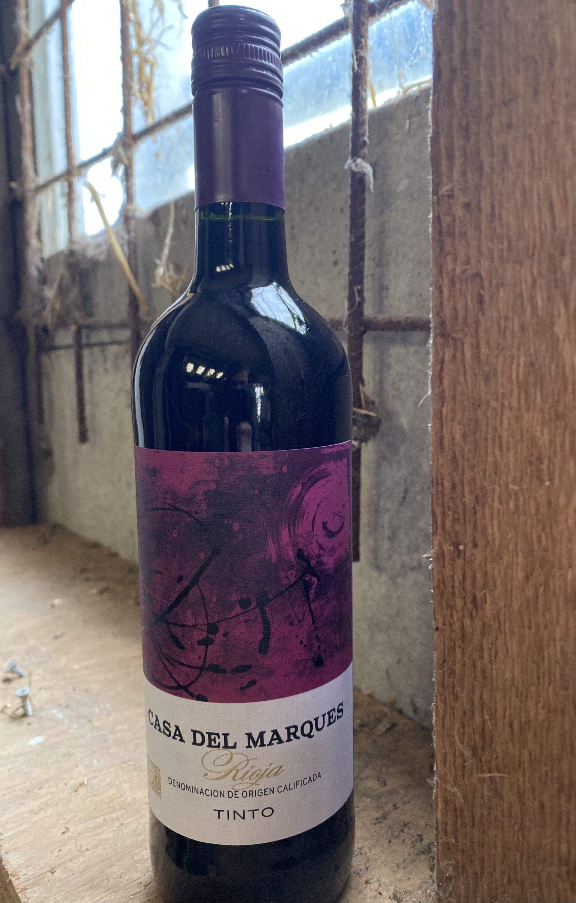 Wijnfles met paars etiket, Casa del Marques Rioja, op een vensterbank tegen een verweerde achtergrond.