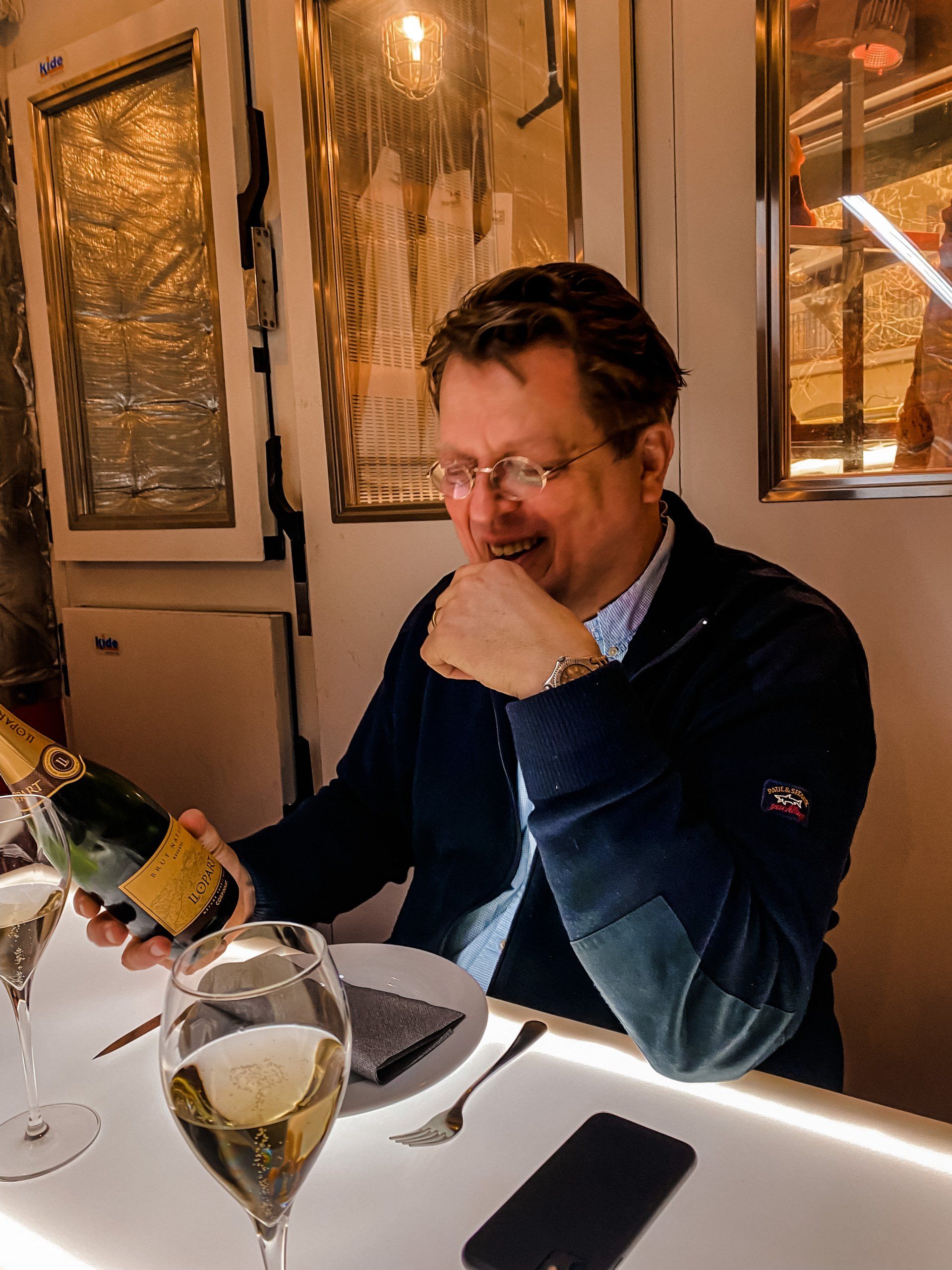 Een man met een bril schenkt champagne in aan een tafel in een restaurant.