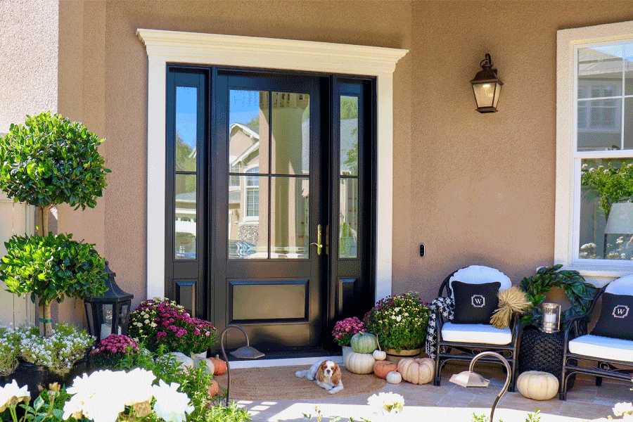 Black front door with sidelights, decorated porch with pumpkins, plants, and wicker chairs. Black front door with sidelights, decorated porch with pumpkins, plants, and wicker chairs.