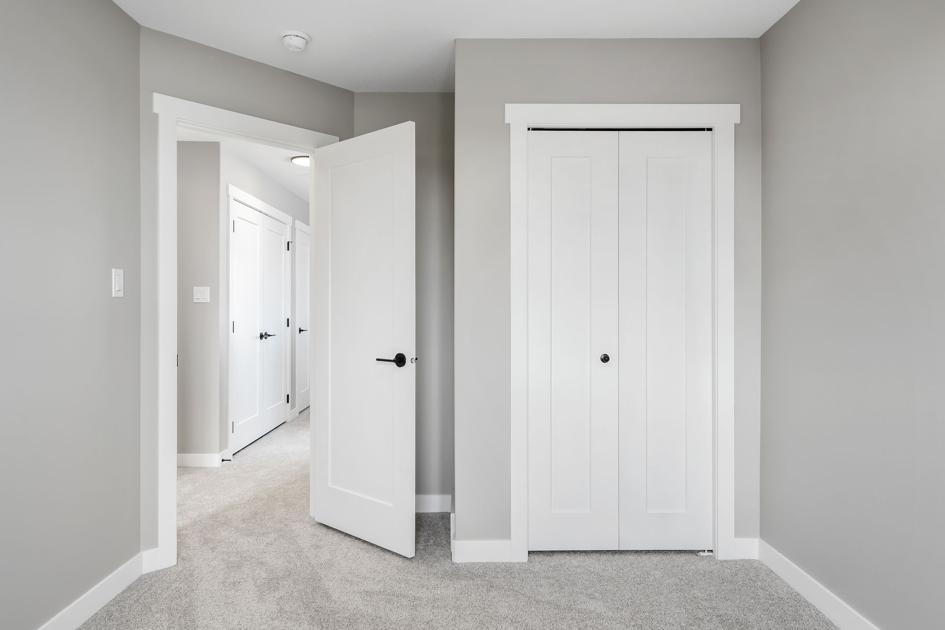 Empty room with gray walls, white trim, two white doors, and light gray carpet.