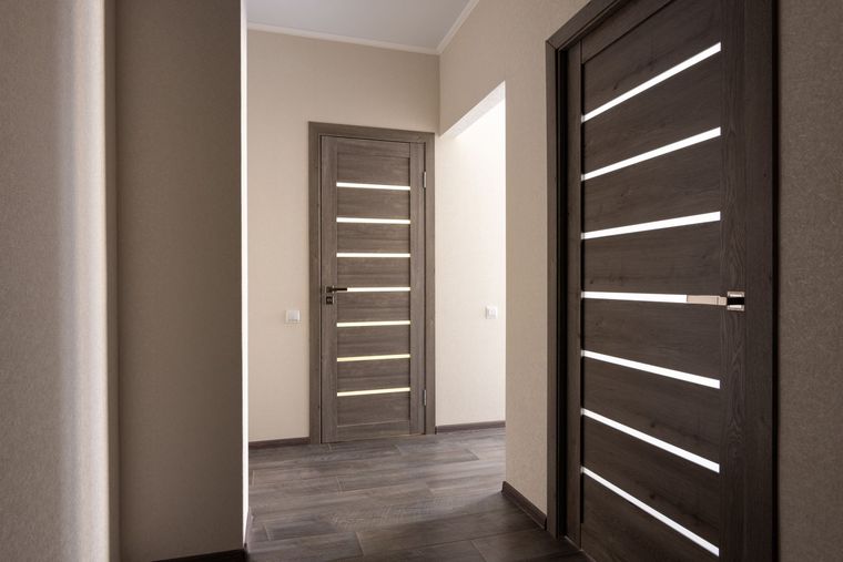 Hallway with three closed wooden doors, gray walls, and dark flooring. Hallway with three closed wooden doors, gray walls, and dark flooring.
