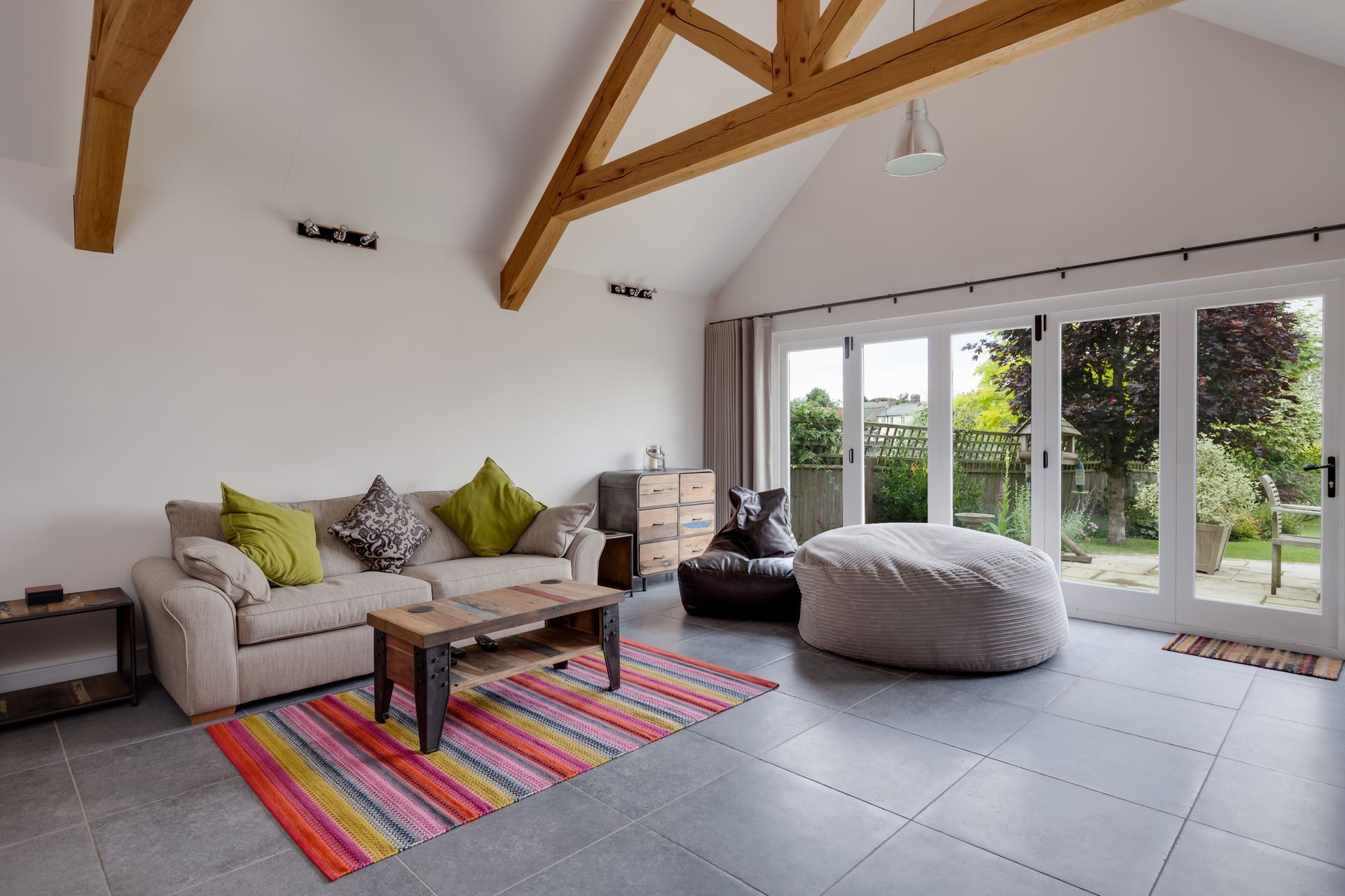 Living room with cream sofa, colorful rug, sliding doors, and exposed wooden beams.