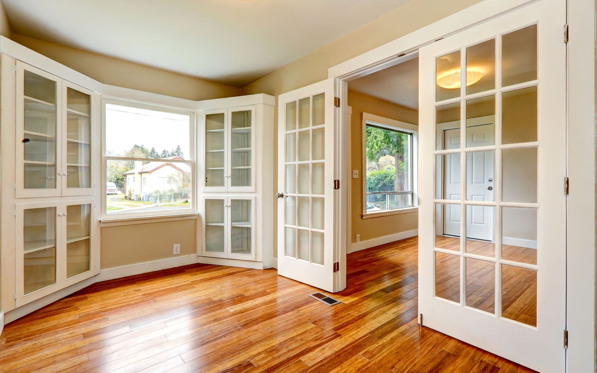 Empty room with hardwood floors, built-in white cabinets, and French doors.