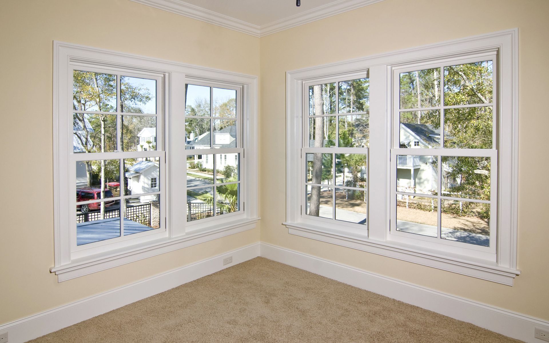 Corner of a room with two sets of white-framed windows, beige walls, and tan carpet.