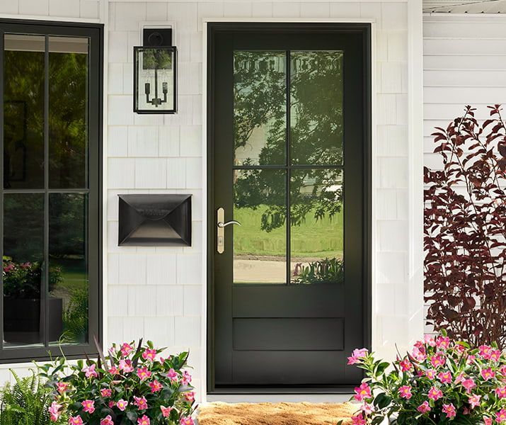 Black front door with glass panels, brass handle, and black lantern on a white shingled exterior. Black front door with glass panels, brass handle, and black lantern on a white shingled exterior.