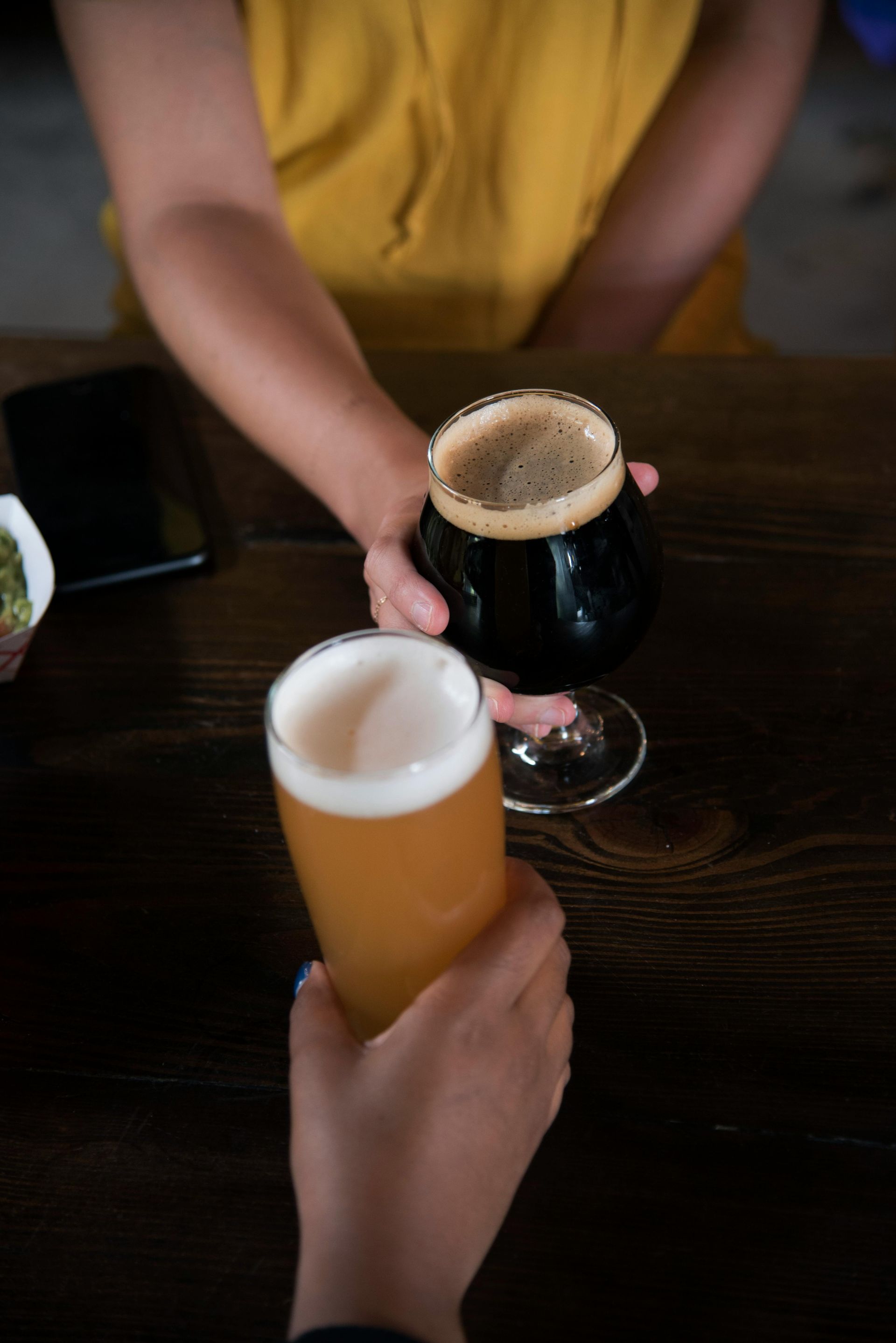 Two people are holding glasses of beer on a table.