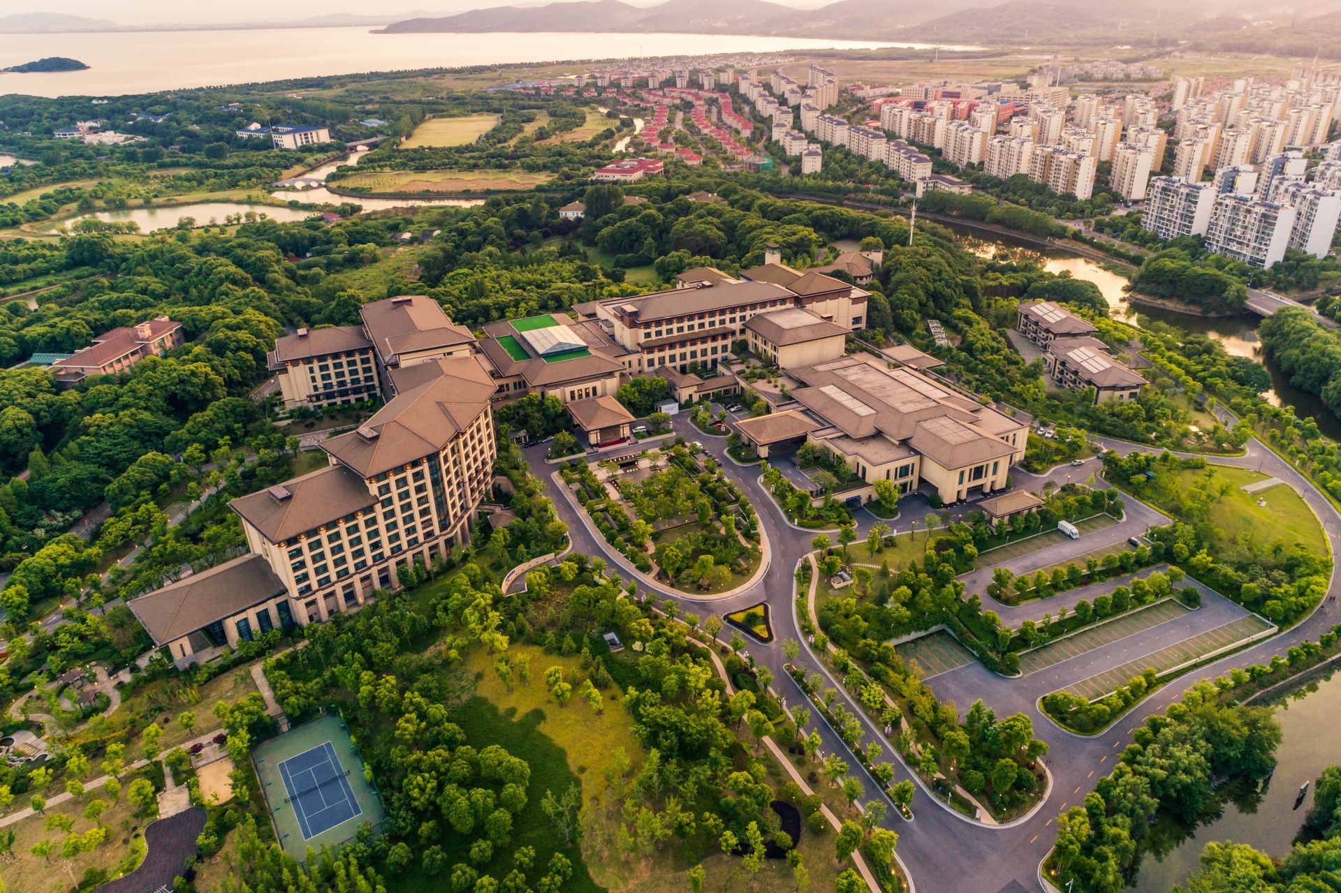 Aerial view of a large campus with buildings, roads, and lush green landscaping near a city skyline