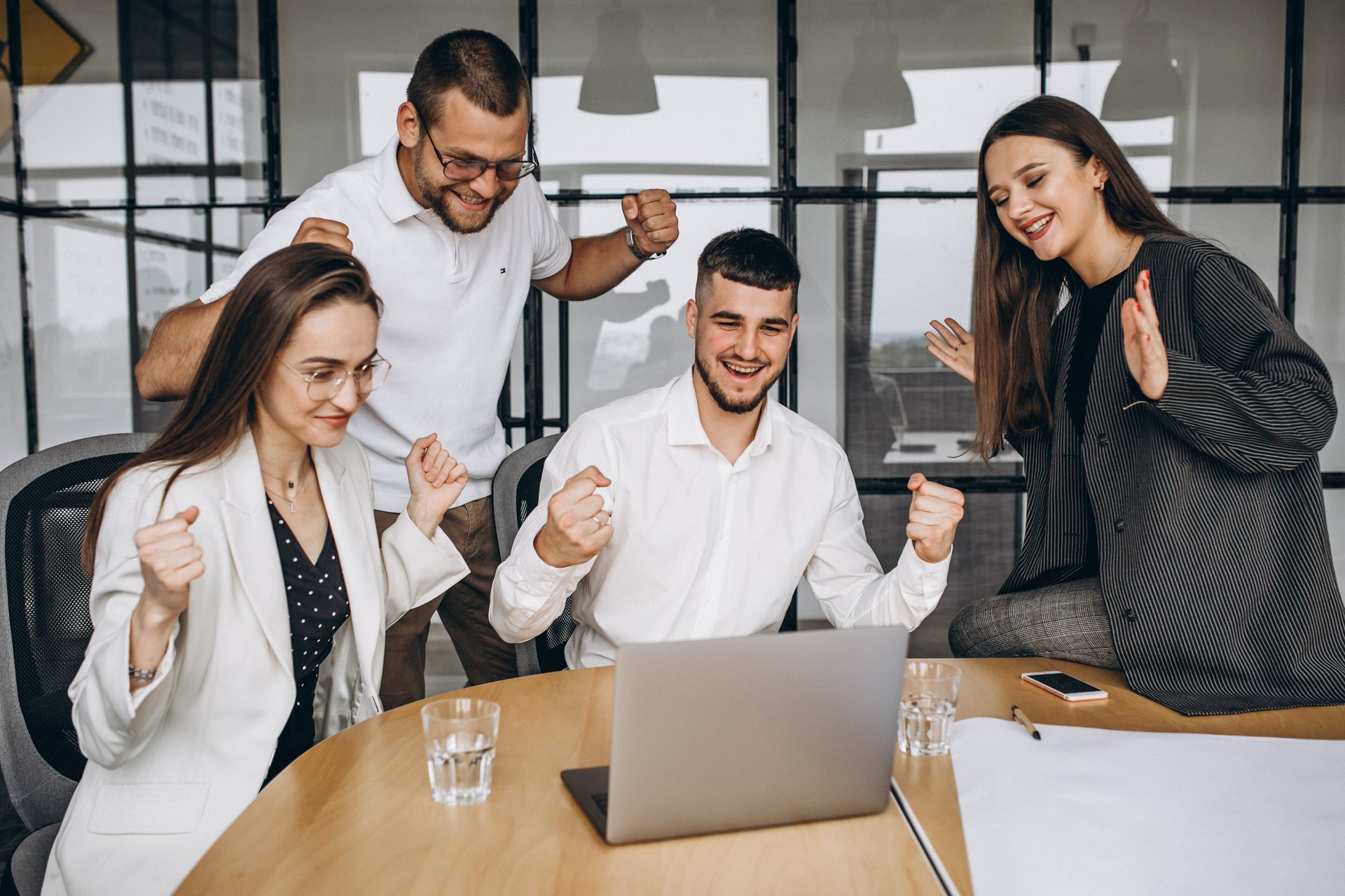 Team celebrating around a laptop in a bright office meeting room