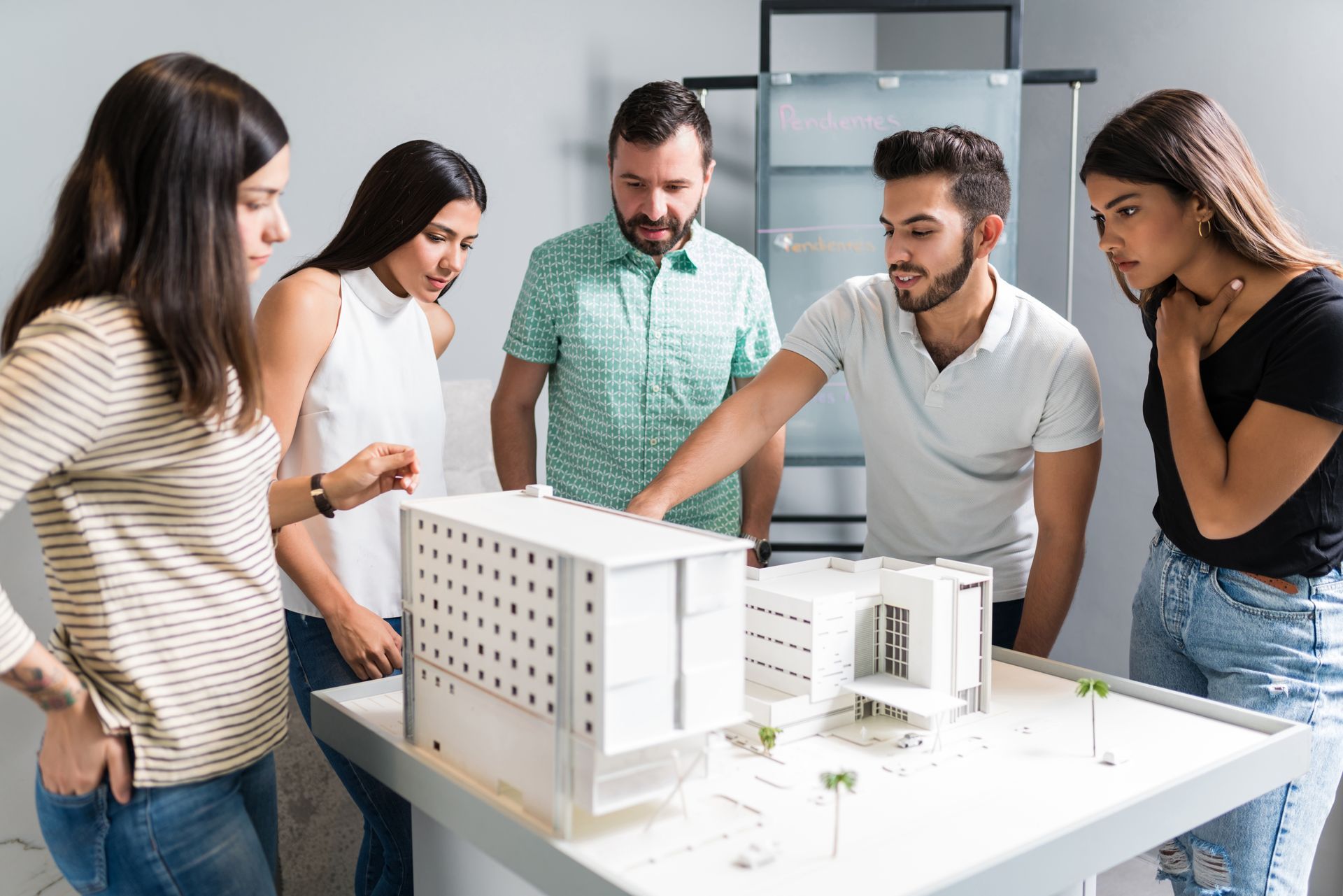 People examining a white architectural model on a table in a bright office.