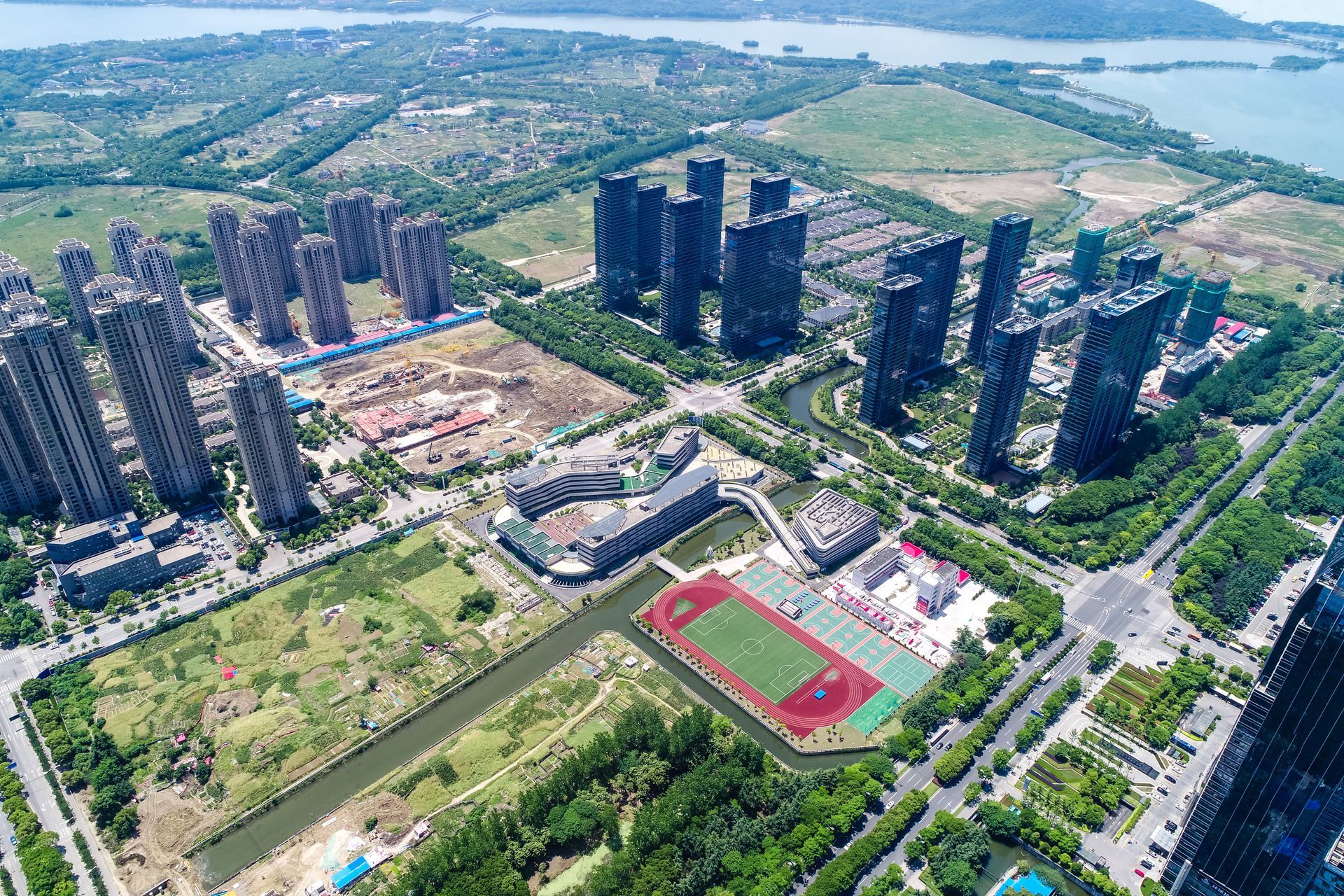 Aerial view of modern high-rise apartments, a red sports field, and green parkland near water