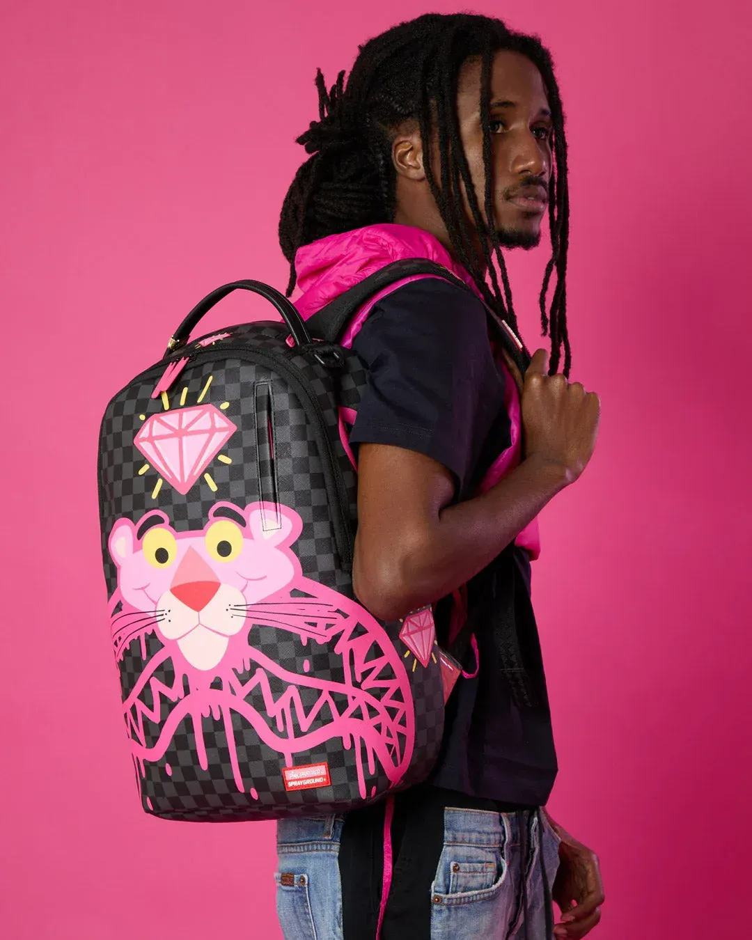 Persona con i dreadlocks che porta uno zaino nero e rosa su sfondo rosa