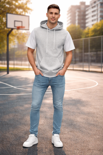 Un uomo in piedi su un campo da basket all'aperto indossa una felpa grigia con cappuccio, jeans e scarpe da ginnastica bianche.