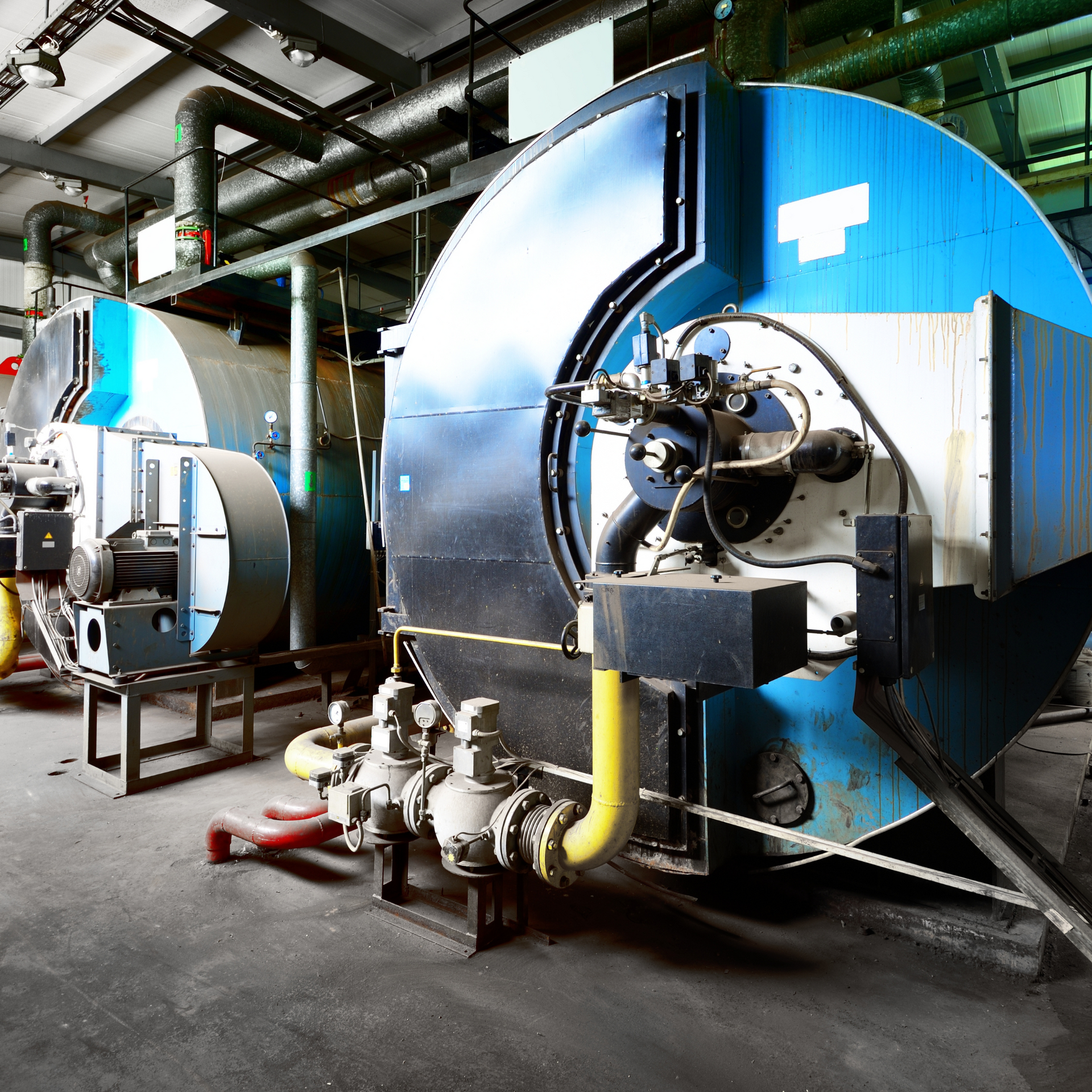 Two large blue industrial boilers in a factory setting with various pipes and controls.