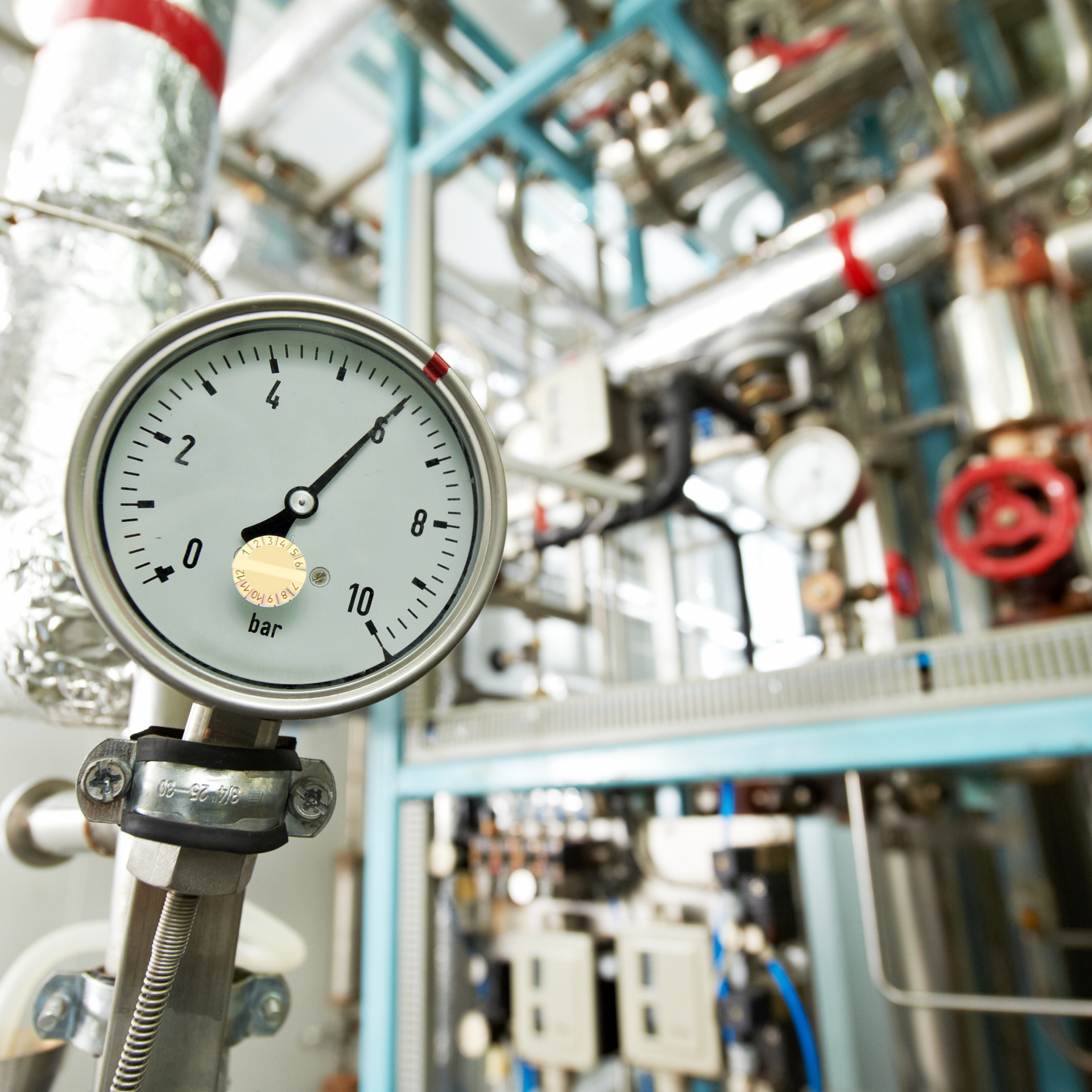 Pressure gauge in industrial setting, indicating pressure between 8 and 9.