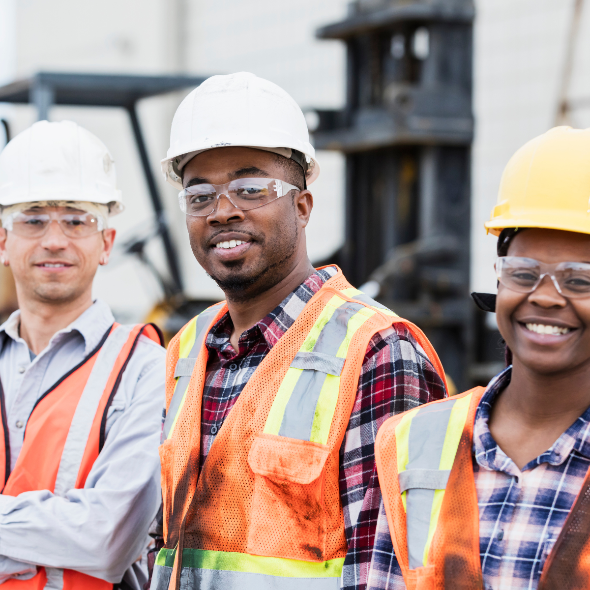Construction workers smiling at the camera, wearing hard hats, safety glasses, and vests.