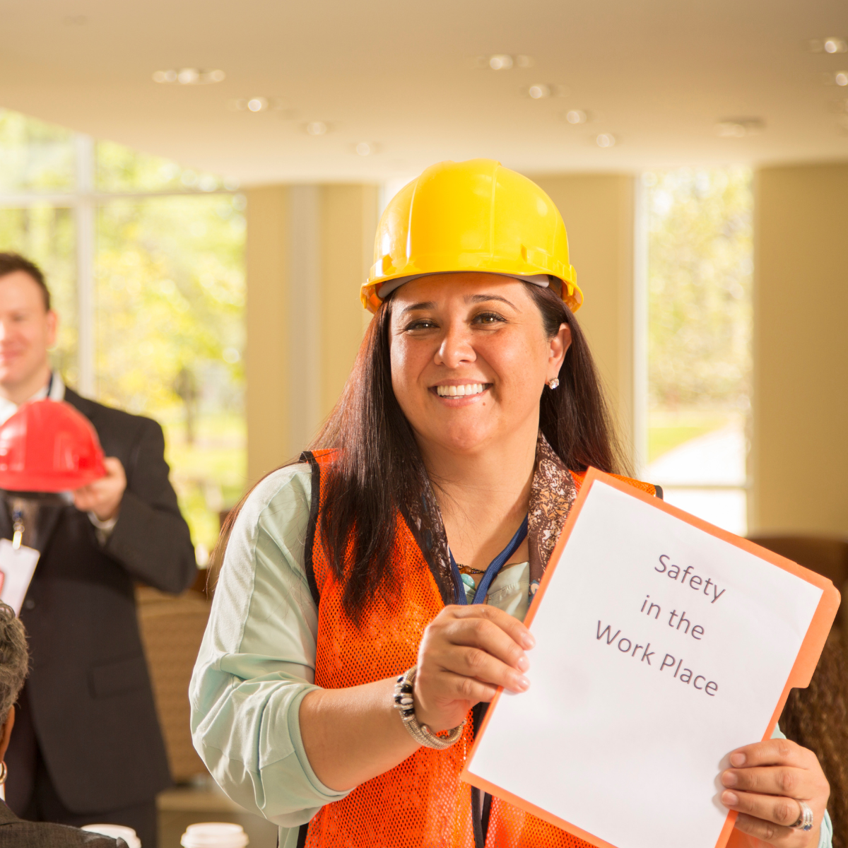 Woman in hard hat and vest smiles, holding 