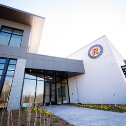 Modern office building with gray and white facade, a large logo, and walkway.