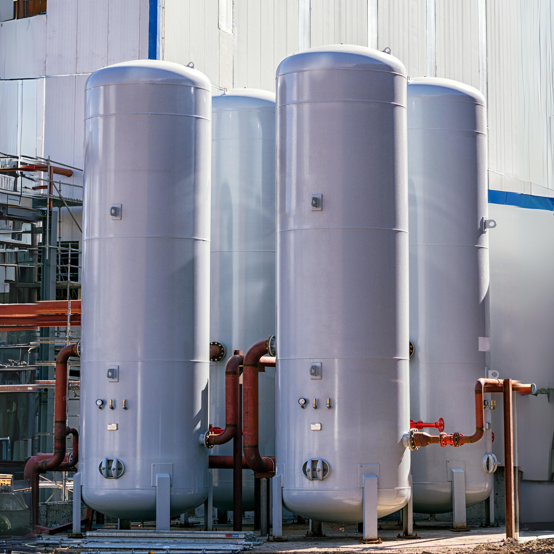 Large, cylindrical gray storage tanks with rust-colored pipes, outdoors.
