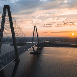 A cable-stayed bridge spans a river at sunset; golden sky, water, and city in the background.