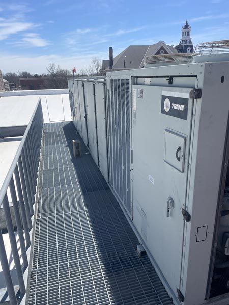Rooftop HVAC units beside a metal walkway under a clear blue sky.