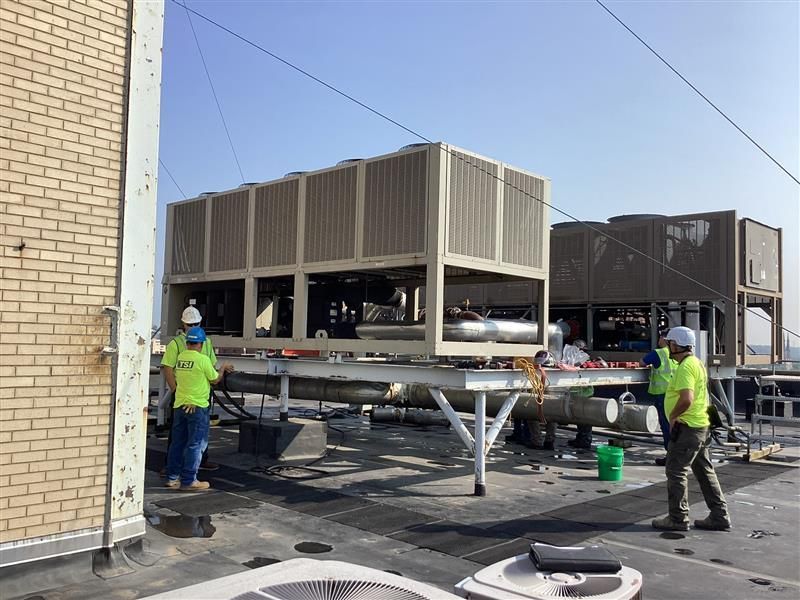 Workers in hard hats moving a large rooftop HVAC unit on a building roof