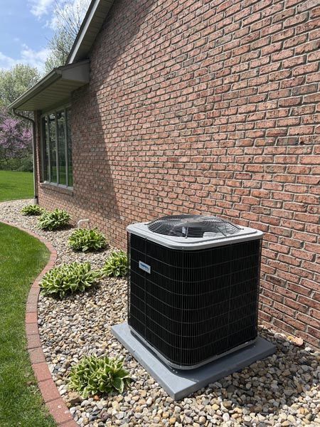 Outdoor HVAC unit beside a brick house, next to a window and landscaped gravel bed