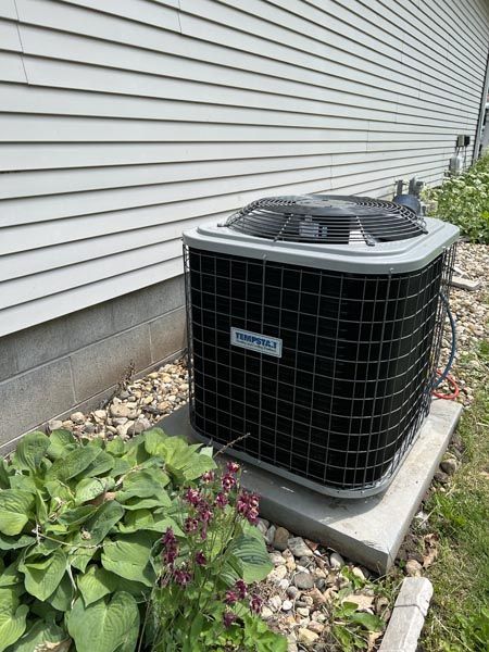 Outdoor central air conditioner beside a house, with white siding and rocks around the base.