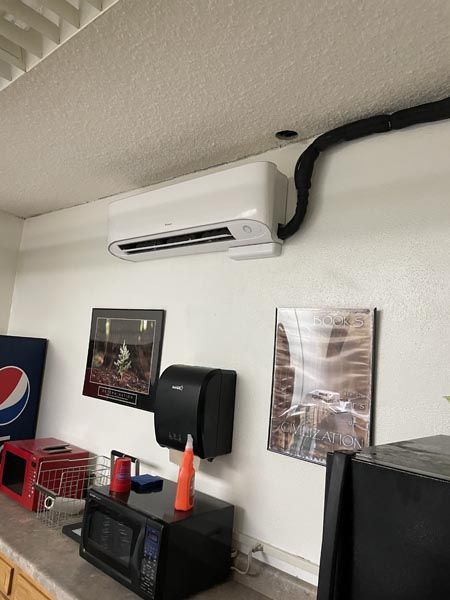 Wall-mounted air conditioner above a black dispenser and posters on a white indoor wall
