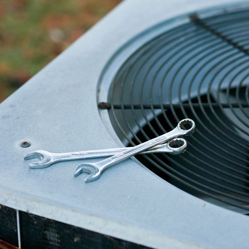 Two silver wrenches resting on the top of an outdoor air conditioner unit