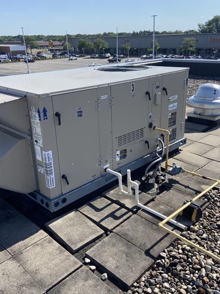 Rooftop HVAC unit with ductwork and pipes on a flat commercial roof under a clear sky