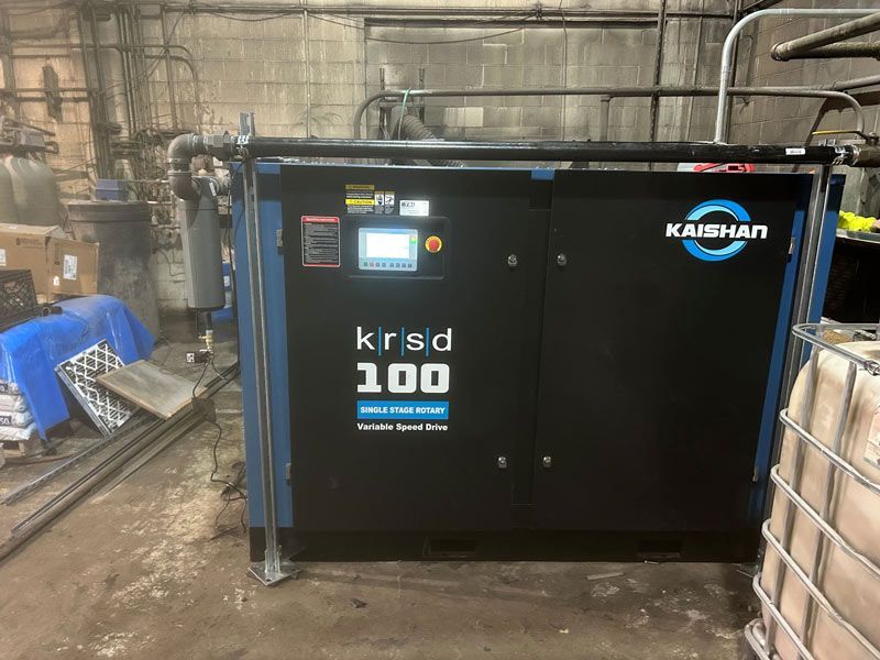 Black Kaishan air compressor in an industrial room with pipes and brick walls