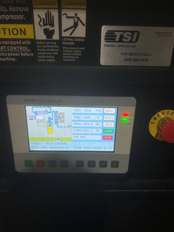 Industrial control panel with touchscreen display, warning labels, and a red emergency stop knob on the right.