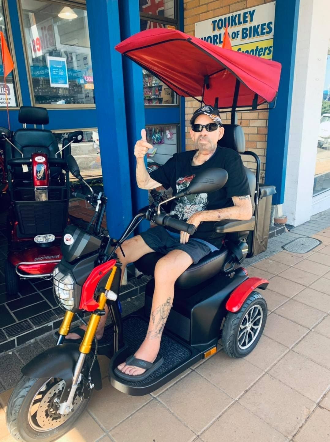 A Man Is Sitting on A Scooter with A Red Canopy and Giving a Thumbs Up — Toukley World of Bikes In Toukley, NSW