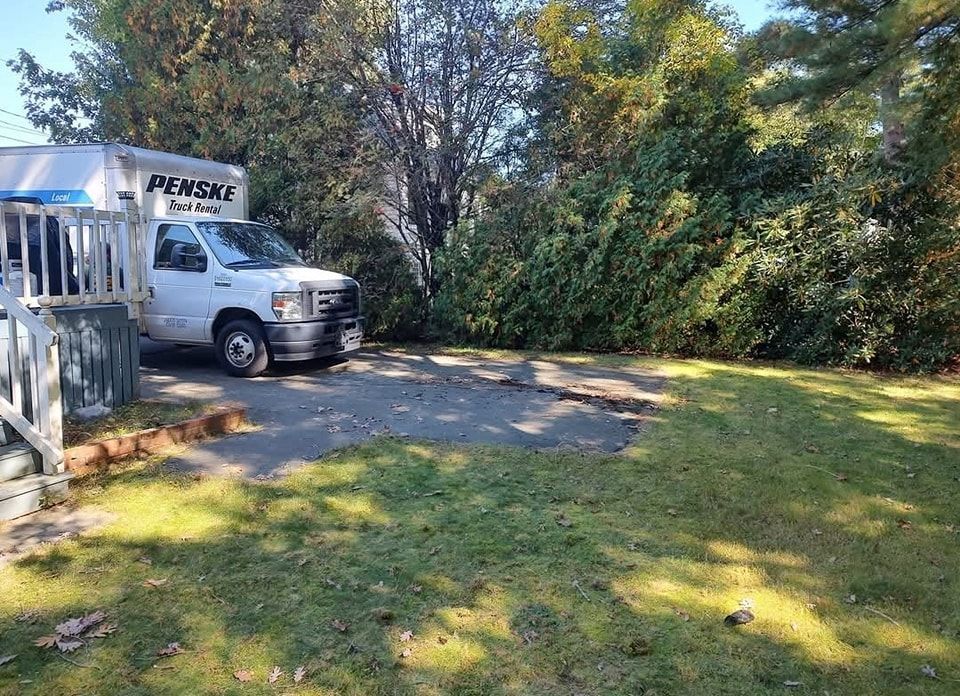 Penske moving truck parked by a driveway beside a grassy yard and trees