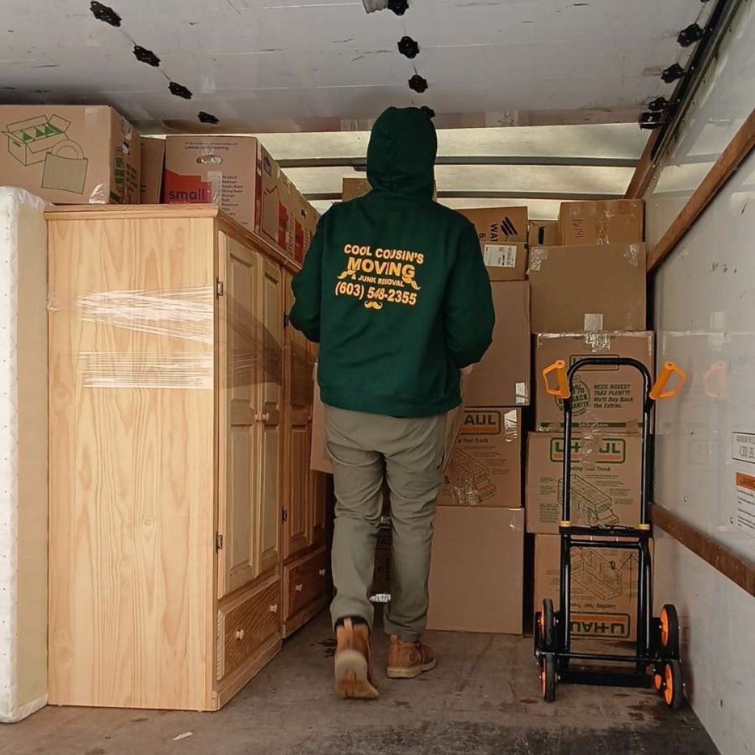 Mover in green hoodie walks inside a packed moving truck with boxes and furniture.
