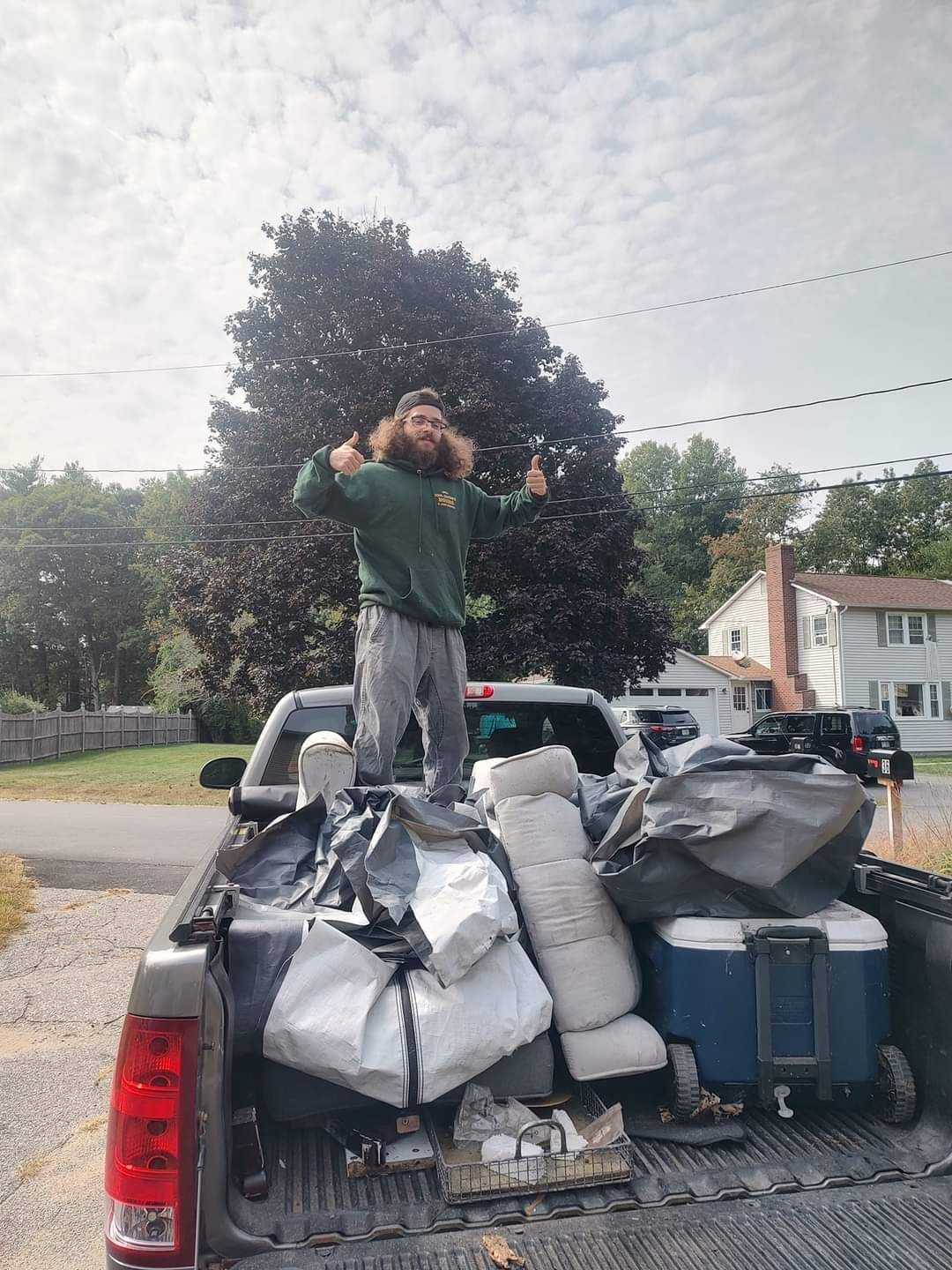 Person standing in a pickup truck bed piled high with bags and luggage on a residential street