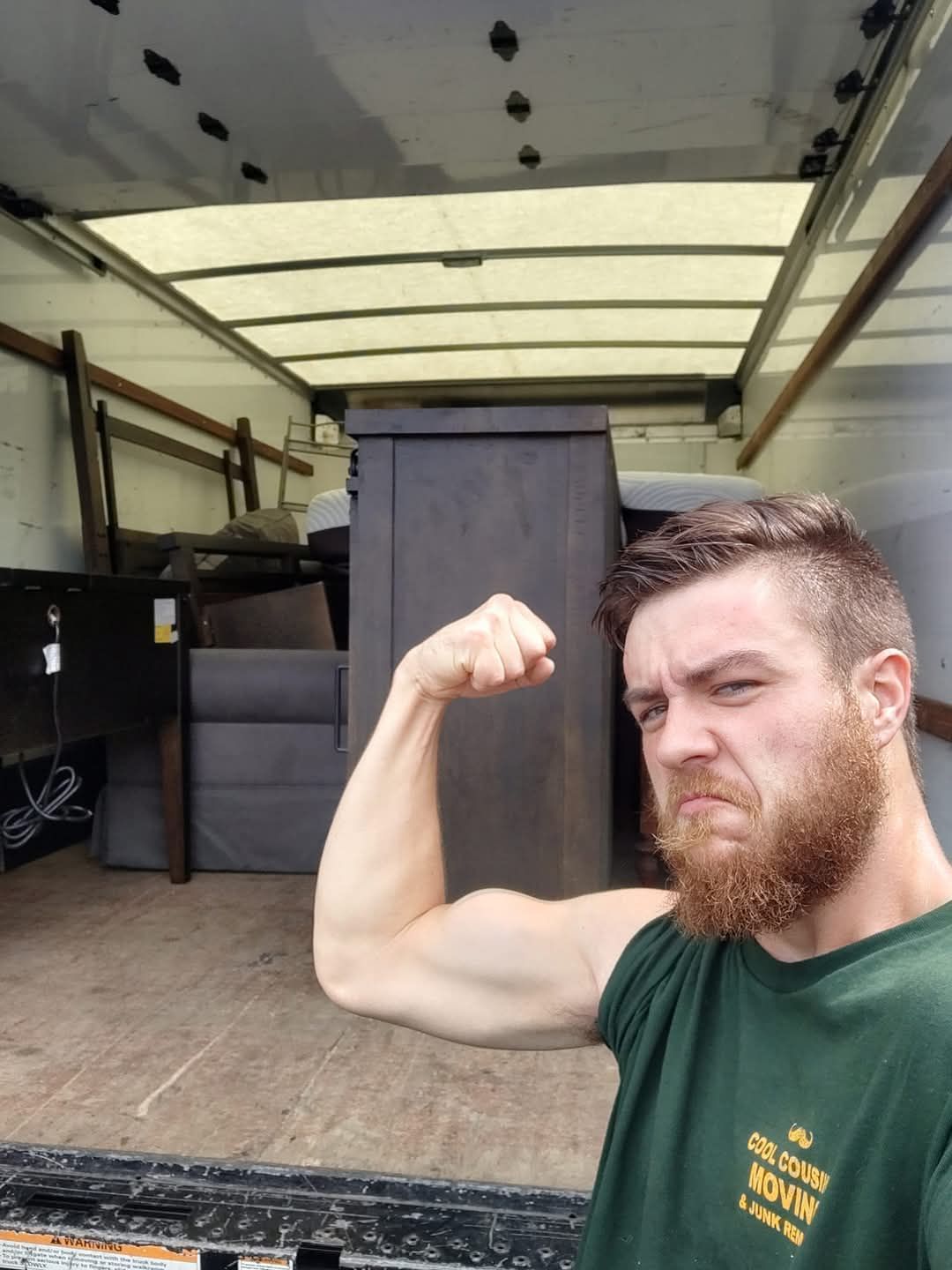Man flexing his arm in front of a moving truck loaded with furniture boxes