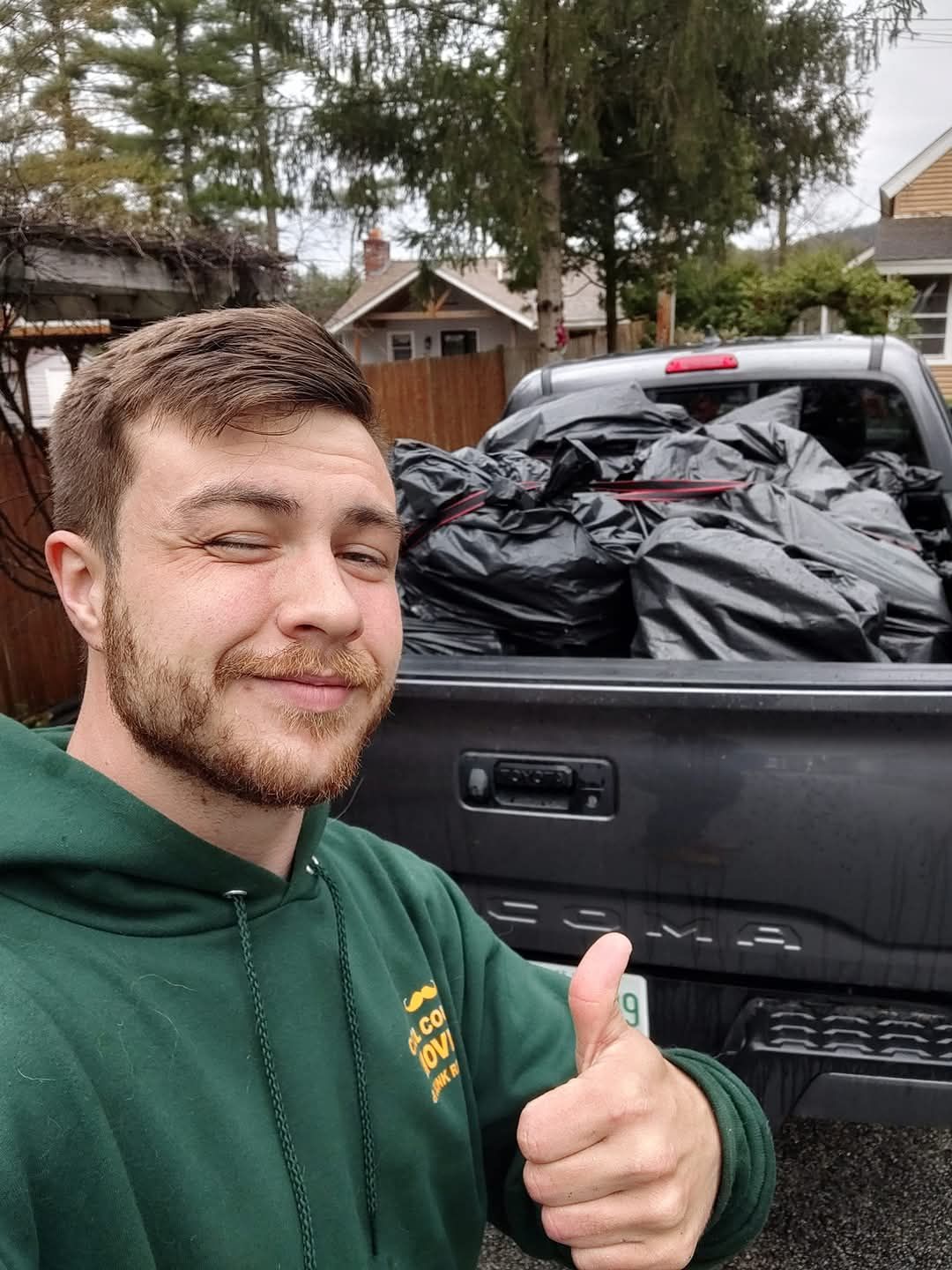 Man smiling and giving a thumbs-up beside a pickup truck loaded with black bags outdoors