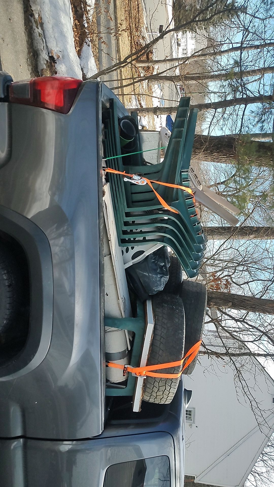Gray pickup truck loaded with stacked green metal chairs and orange straps in a driveway