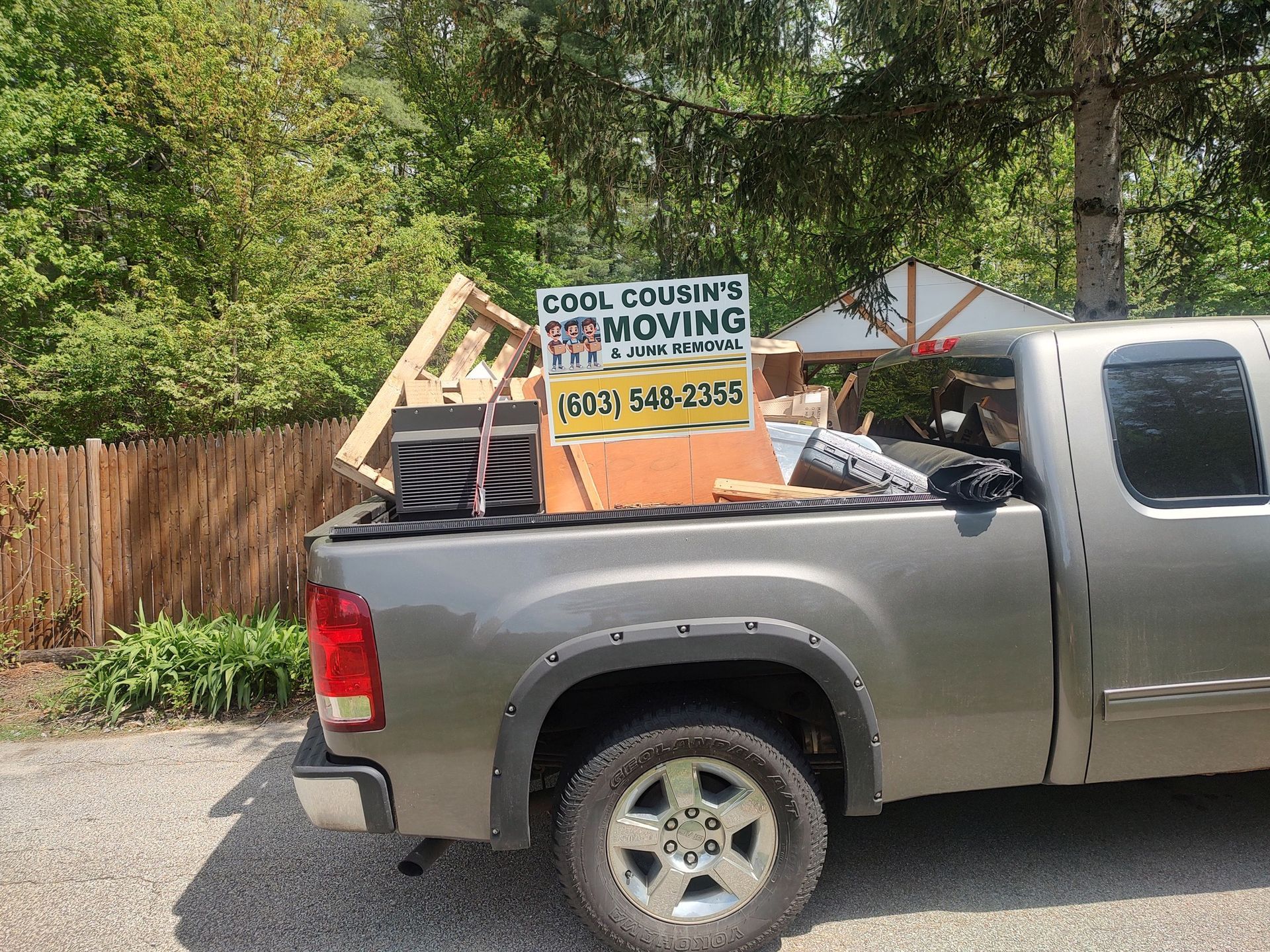 Silver pickup truck loaded with debris and a moving sign parked on a residential street